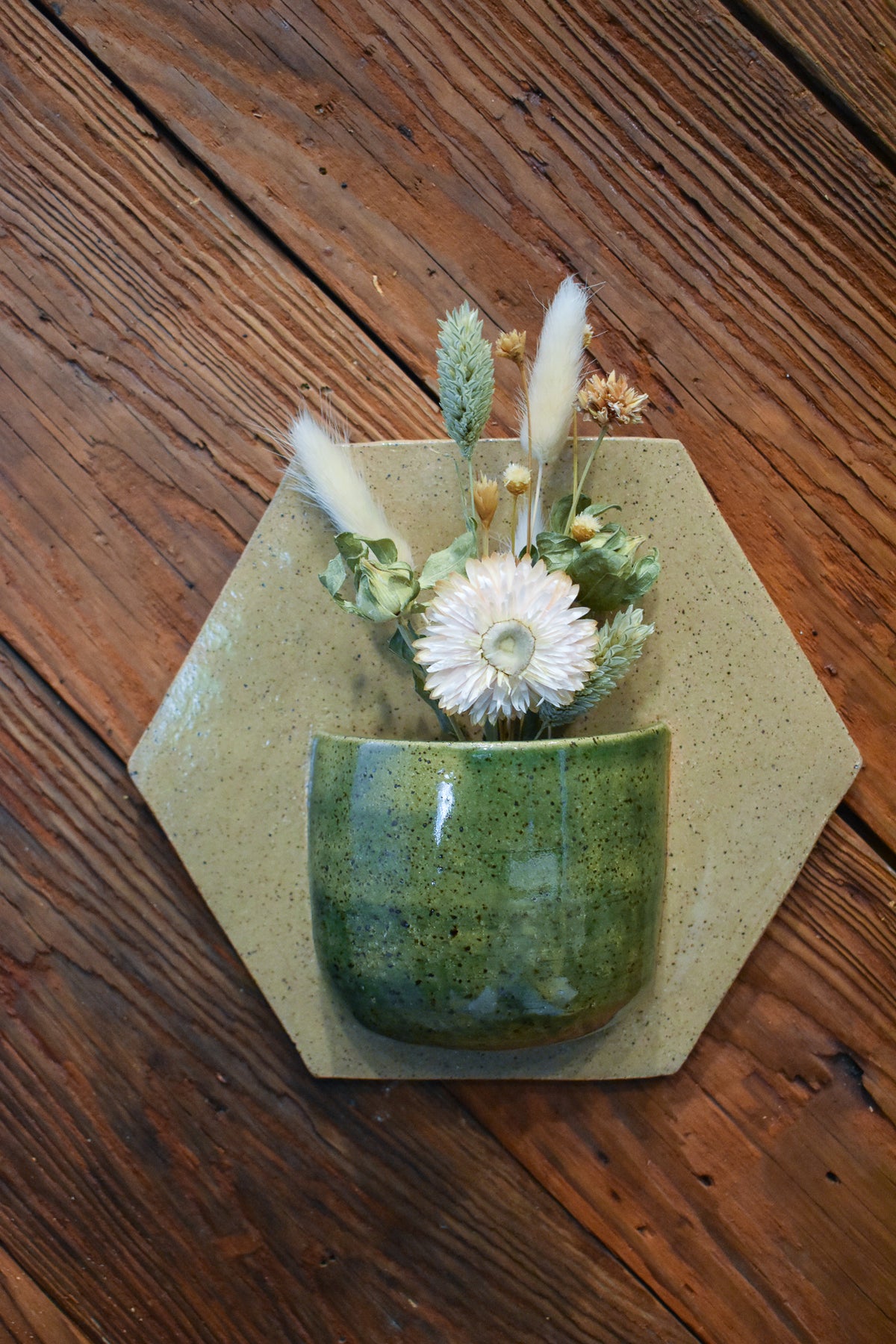 Medium hand-formed wall vase in Woodland, a glossy forest-green pocket on an oatmeal hexagon back plate