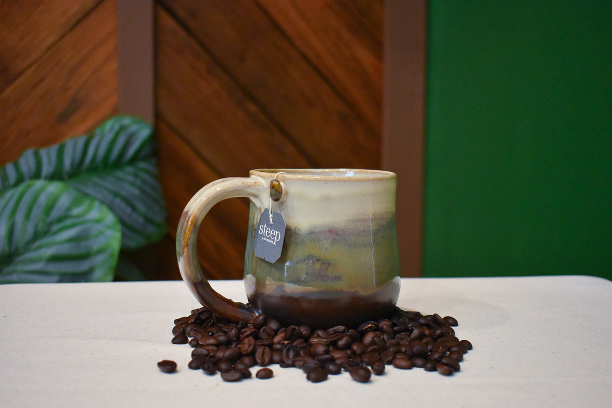 Hand-thrown mug in Autumn Hills, cream over olive and moss streaked with rust, settling to chocolate brown