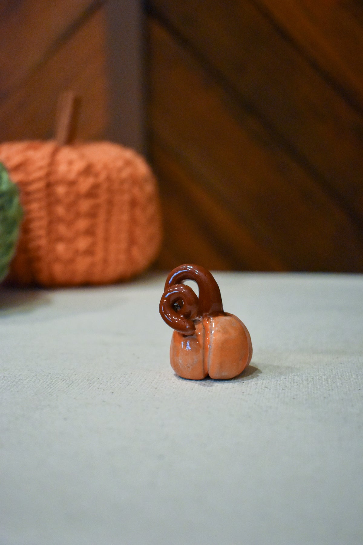 Hand-sculpted ceramic pumpkin in glossy persimmon orange with a curl of rust-brown vine