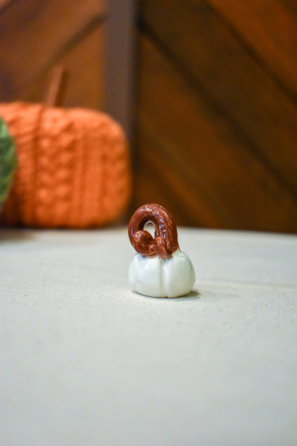 Tiny hand-sculpted ceramic pumpkin in glossy moonstone white with a curl of rust-brown vine