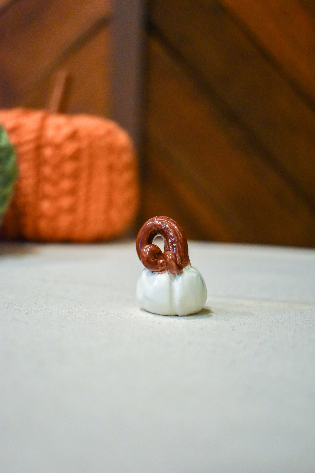 Tiny hand-sculpted ceramic pumpkin in glossy moonstone white with a curl of rust-brown vine