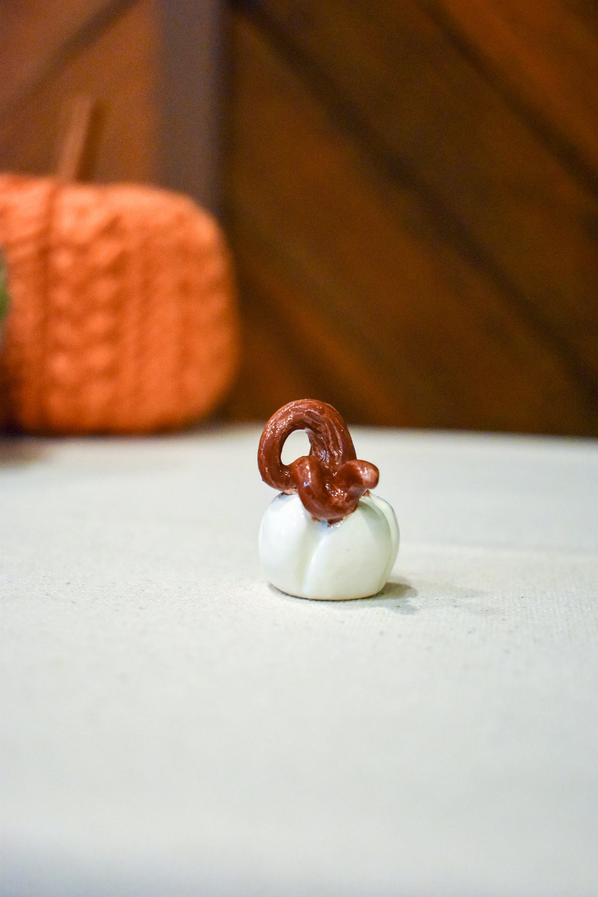 Tiny hand-sculpted ceramic pumpkin in glossy moonstone white with a curl of rust-brown vine