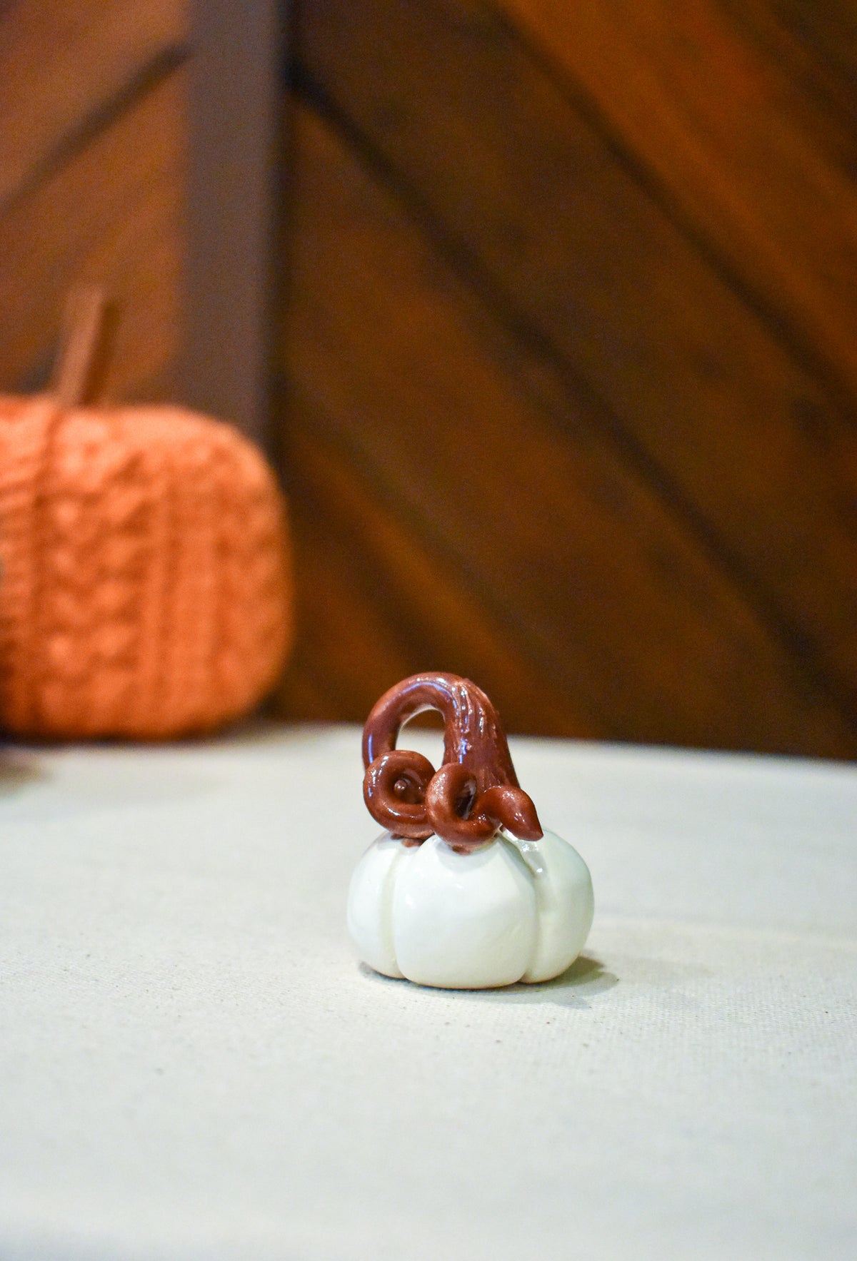 Tiny hand-sculpted ceramic pumpkin in glossy moonstone white with a curl of rust-brown vine