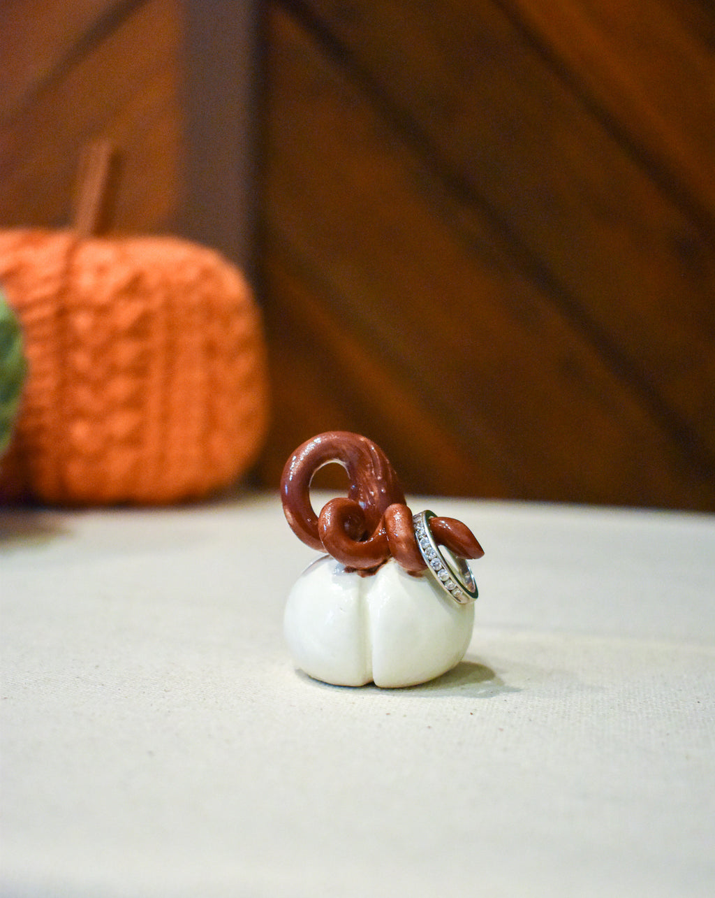 Tiny hand-sculpted ceramic pumpkin in glossy moonstone white with a curl of rust-brown vine