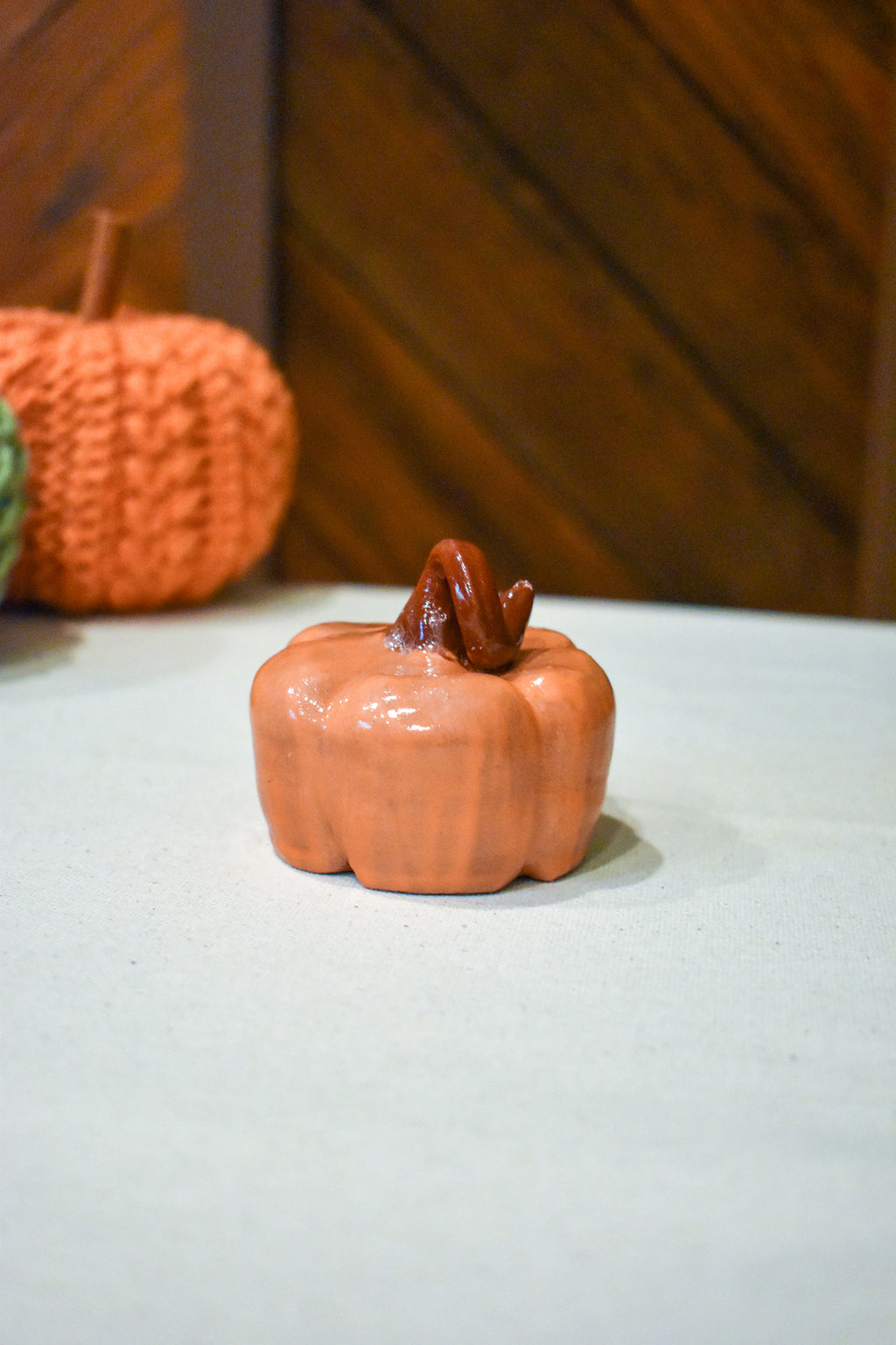 Hand-thrown ceramic pumpkin in glossy persimmon orange with a curl of rust-brown vine