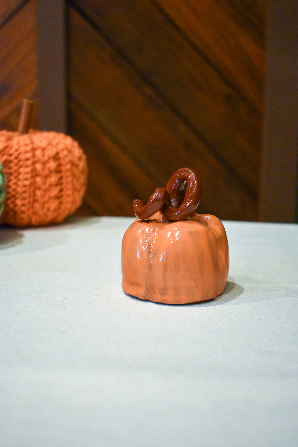 Hand-thrown ceramic pumpkin in glossy persimmon orange with a curl of rust-brown vine