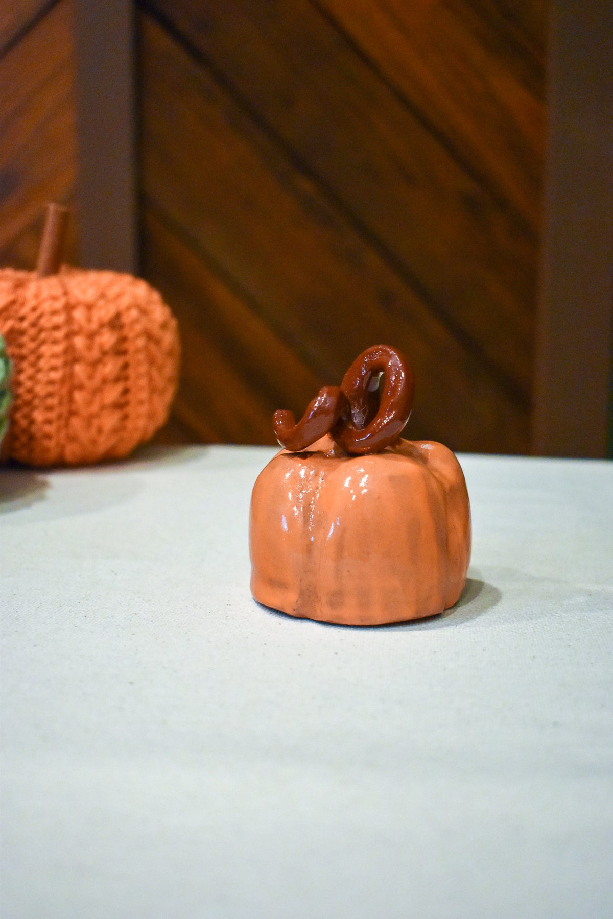 Hand-thrown ceramic pumpkin in glossy persimmon orange with a curl of rust-brown vine