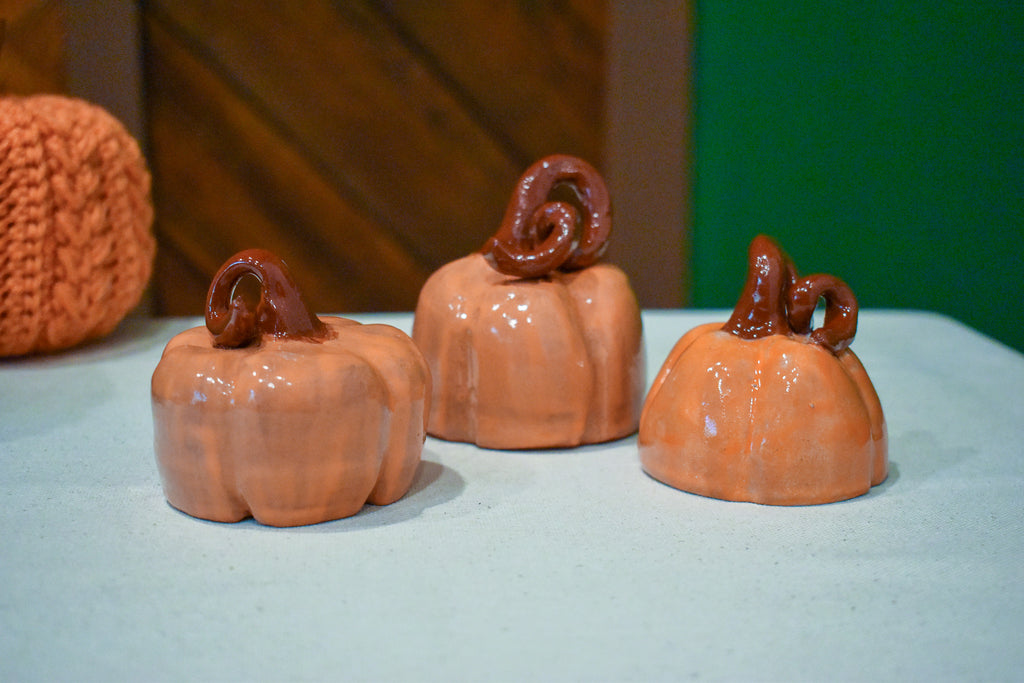 Hand-thrown ceramic pumpkin in glossy persimmon orange with a curl of rust-brown vine