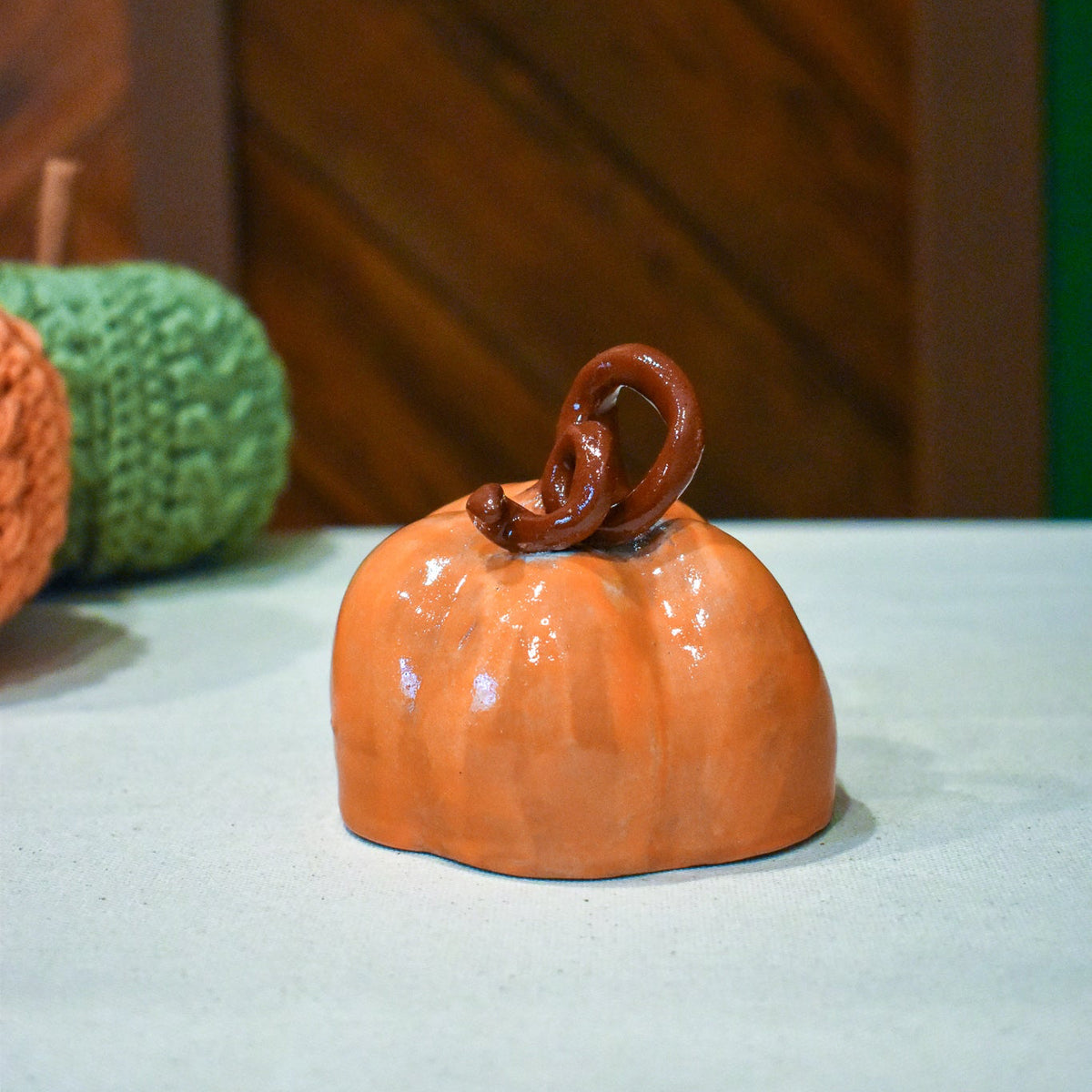 Hand-thrown ceramic pumpkin in glossy persimmon orange with a curl of rust-brown vine
