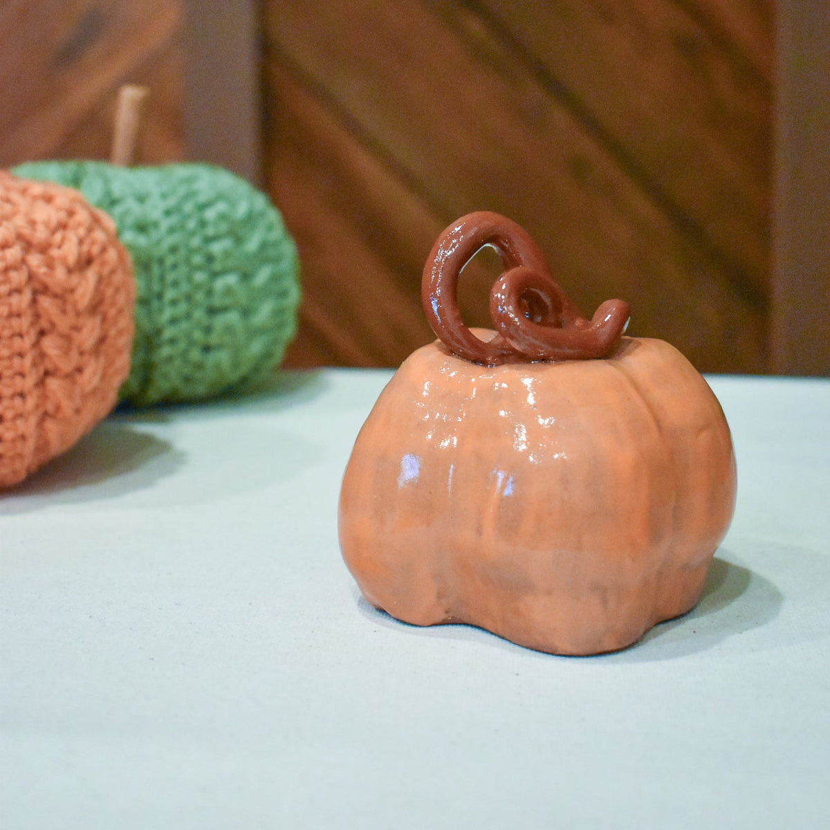 Hand-thrown ceramic pumpkin in glossy persimmon orange with a curl of rust-brown vine