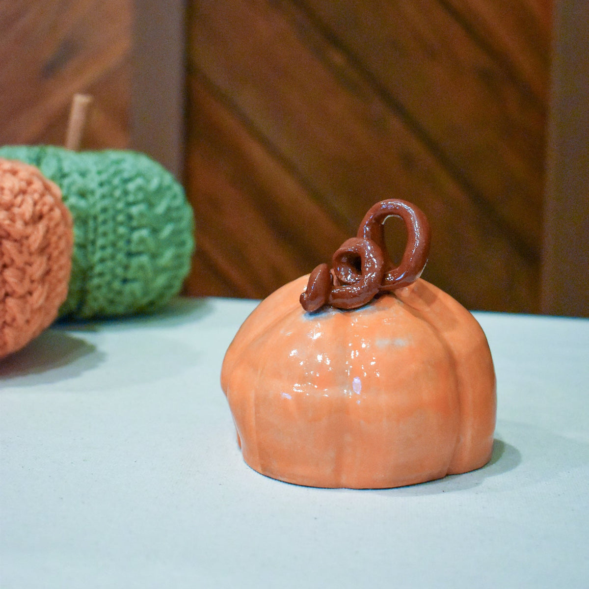 Hand-thrown ceramic pumpkin in glossy persimmon orange with a curl of rust-brown vine