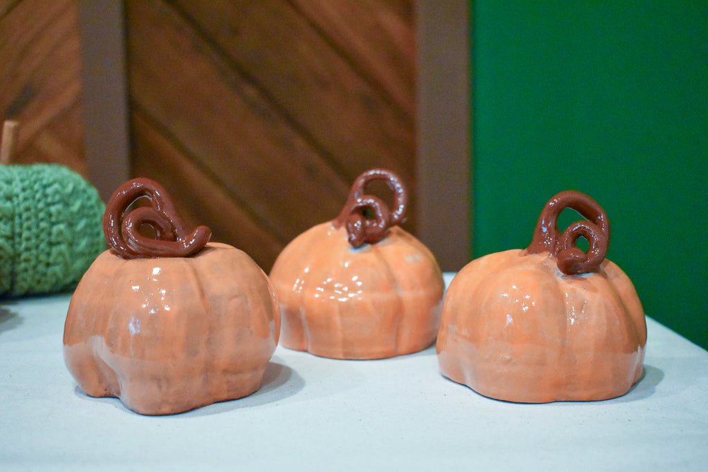Hand-thrown ceramic pumpkin in glossy persimmon orange with a curl of rust-brown vine