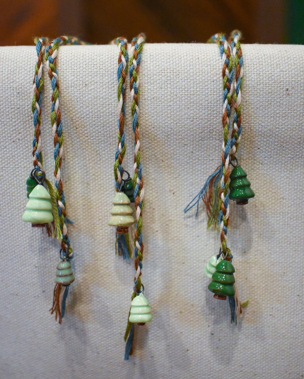 Hand-braided bookmark with hand-sculpted ceramic trees on a braided cord in green, blue, white, and brown