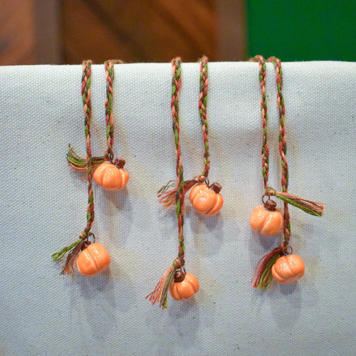 Hand-braided bookmark with hand-sculpted ceramic orange pumpkins on a braided cord in red, orange, brown, and green
