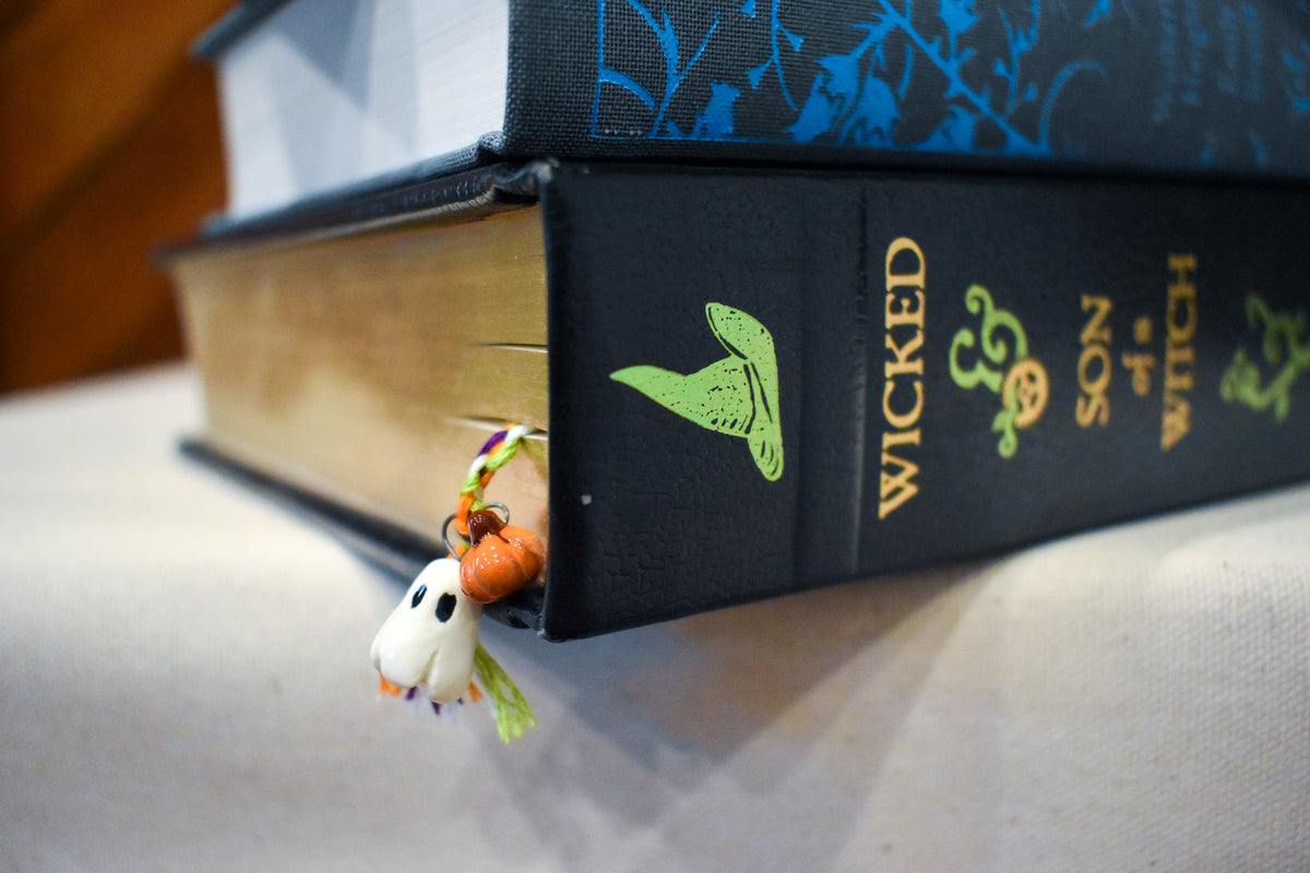 Hand-braided bookmark with a hand-sculpted ceramic ghost and pumpkins on a braided cord in purple, orange, green, and white
