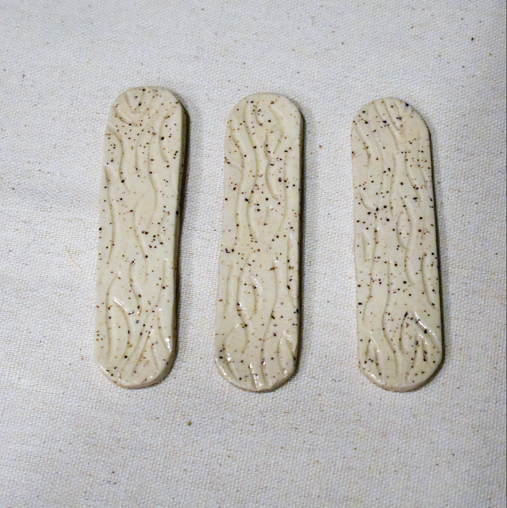 Hand-formed stoneware bookmark with carved wood-grain lines under a creamy white glaze, softly rounded ends