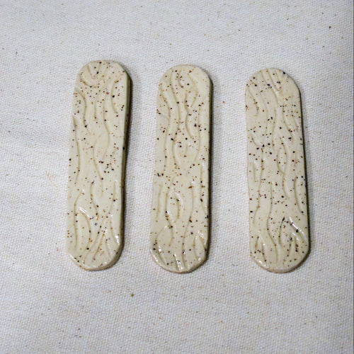 Hand-formed stoneware bookmark with carved wood-grain lines under a creamy white glaze, softly rounded ends