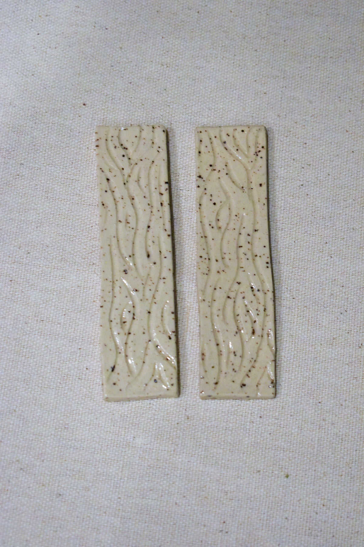 Hand-formed stoneware bookmark with carved wood-grain lines under a creamy white glaze, clean, squared ends