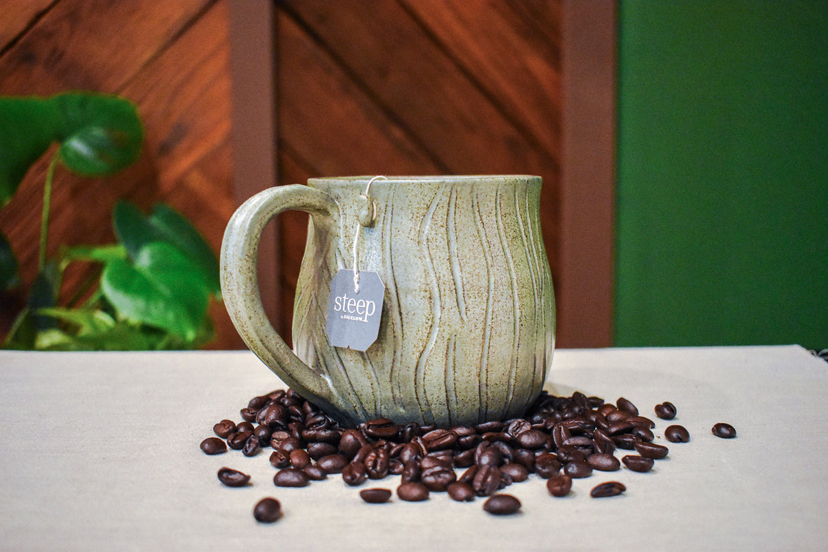 Hand-thrown mug carved with bark-like grain lines in Mosswood, layered sage and warm earth-brown glaze