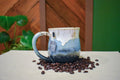 Hand-thrown mug in Snowmelt, cream drips over sky blue deepening to a charcoal base