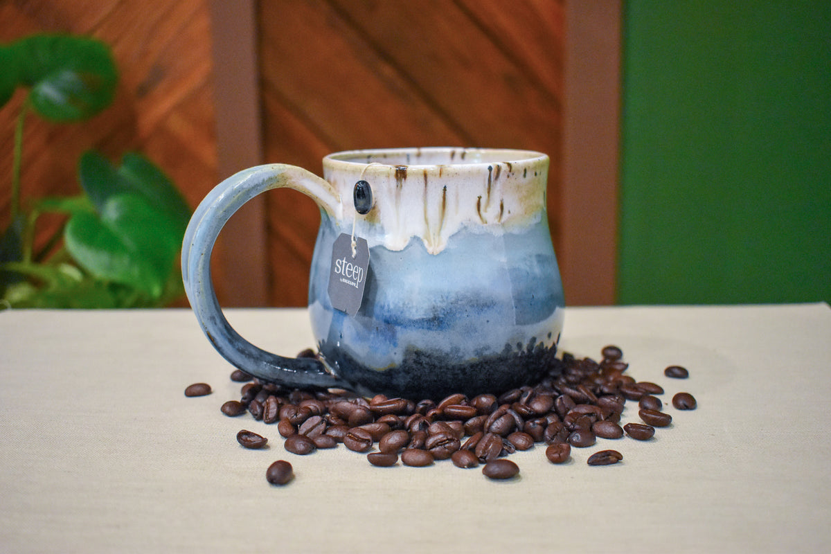 Hand-thrown mug in Snowmelt, cream drips over sky blue deepening to a charcoal base