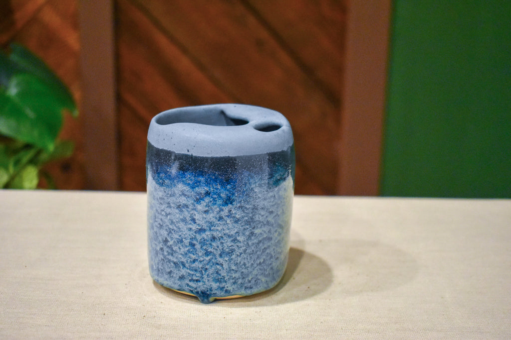 Hand-thrown ceramic travel mug in Blue Drift, matte pale slate blue lid over deep ink blue breaking to pale blue froth over cobalt
