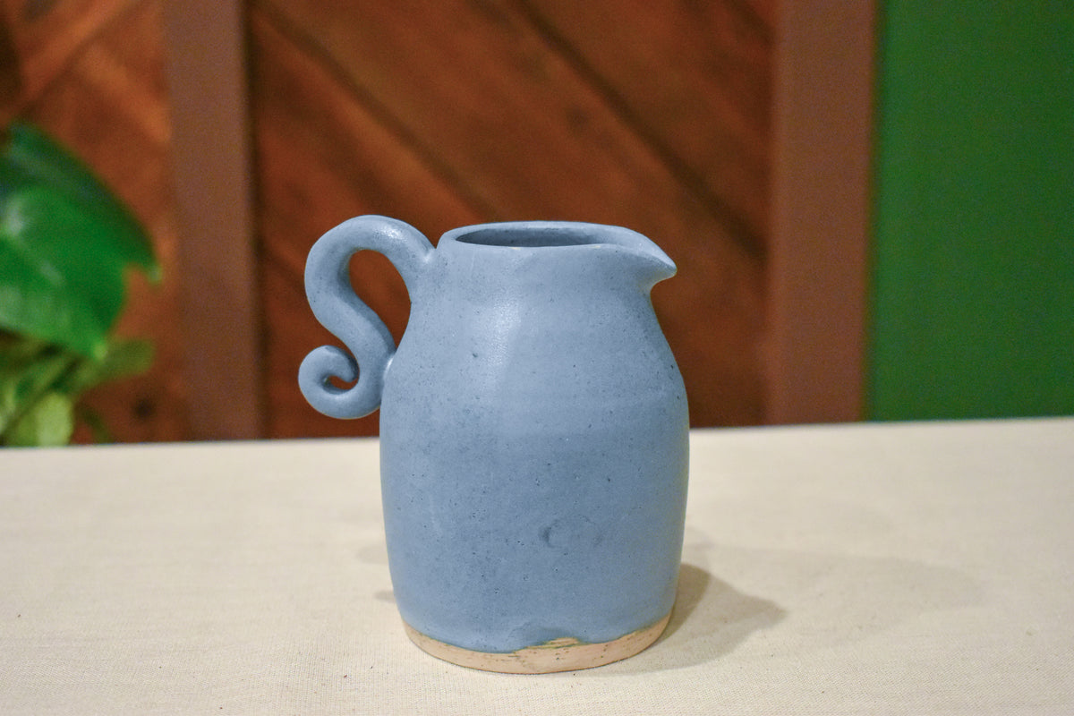 Small hand-thrown pourer in Stillwater with a spout and curled spiral handle, matte slate-blue glaze with raw clay at the foot