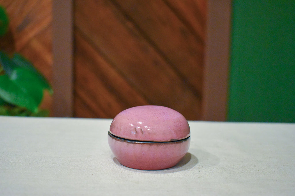 Small hand-thrown lidded jar shaped like a river stone, rosy mauve glaze with a near-black rim