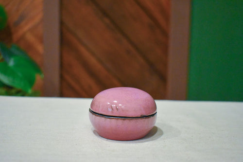 Small hand-thrown lidded jar shaped like a river stone, rosy mauve glaze with a near-black rim