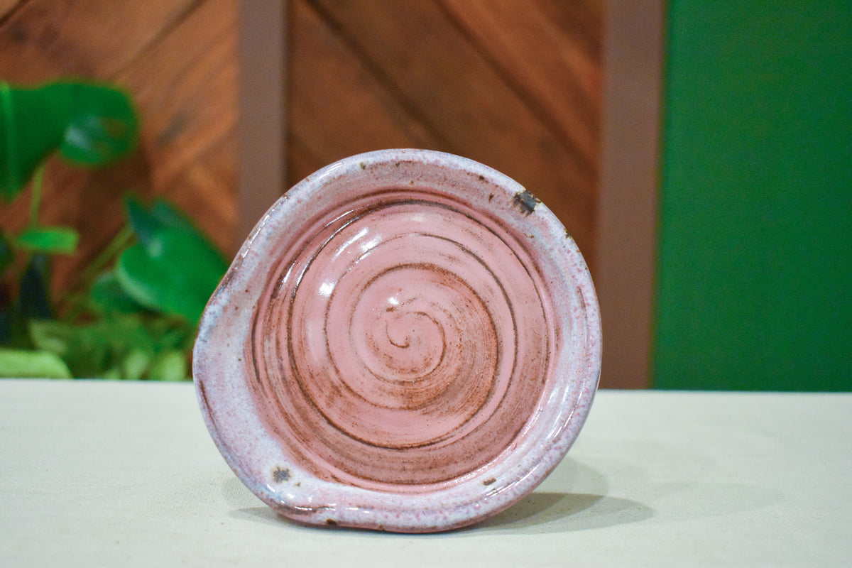 Hand-thrown spiral spoon rest in Soft Blush, warm blush pink with dark clay showing in the spiral and rim