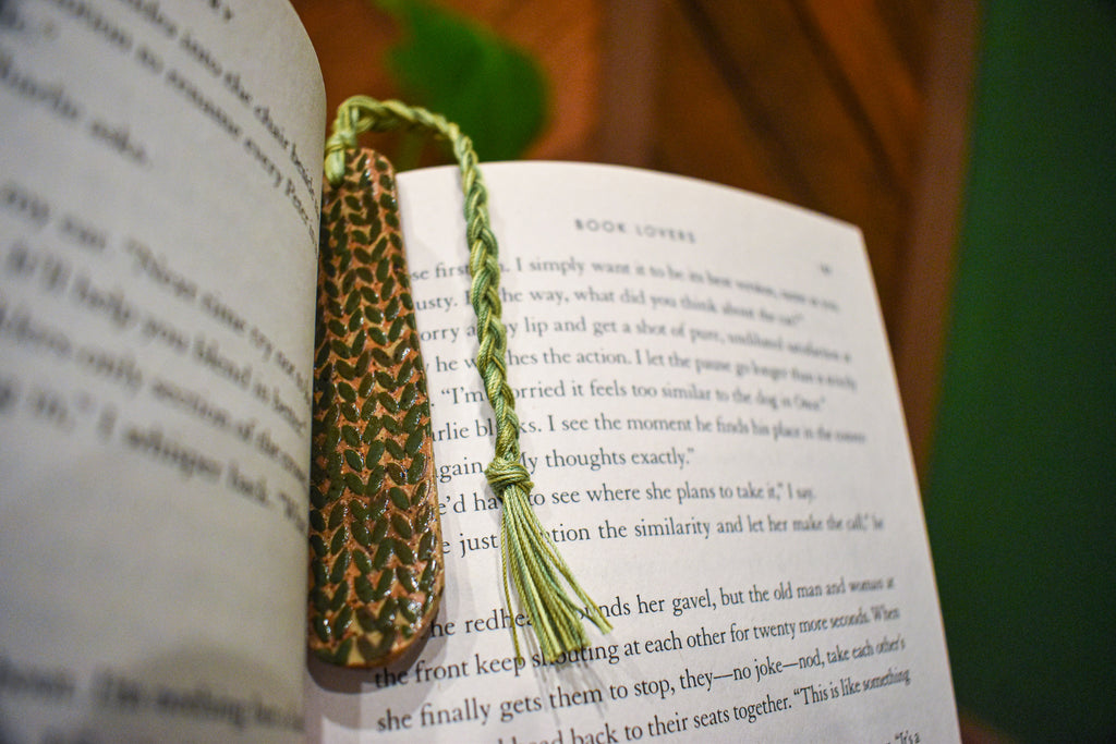 Hand-formed stoneware bookmark with a deep forest-green knit-stitch texture and an olive braided cord