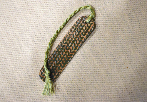 Hand-formed stoneware bookmark with a deep forest-green knit-stitch texture and an olive braided cord