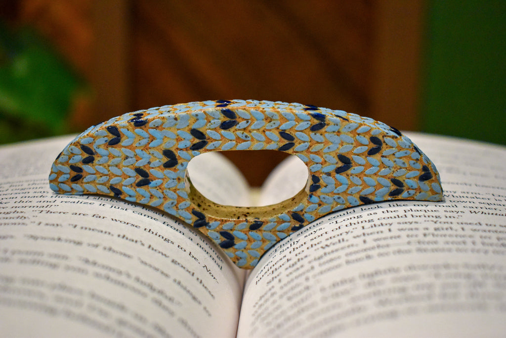 Hand-formed ceramic thumb book holder in Sky Knit, sky-blue knit-stitch texture with navy stitches