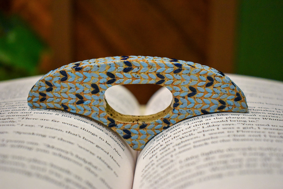 Hand-formed ceramic thumb book holder in Sky Knit, sky-blue knit-stitch texture with navy stitches