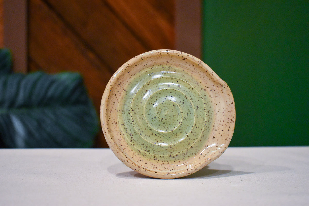 Hand-thrown spiral spoon rest in Sage Pool, soft sage green pooling in the spiral and fading to speckled cream at the rim
