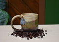 Hand-thrown mug in Autumn Hills, cream over olive and moss streaked with rust, settling to chocolate brown