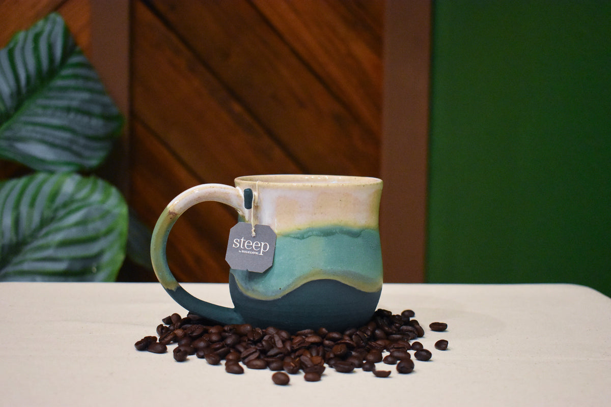 Hand-thrown mug in Lakeshore, warm cream with a gold line over soft aqua and deep matte teal