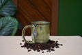 Hand-thrown mug in River Moss, glossy moss green shifting to olive and warm gold with blue flecks near the rim