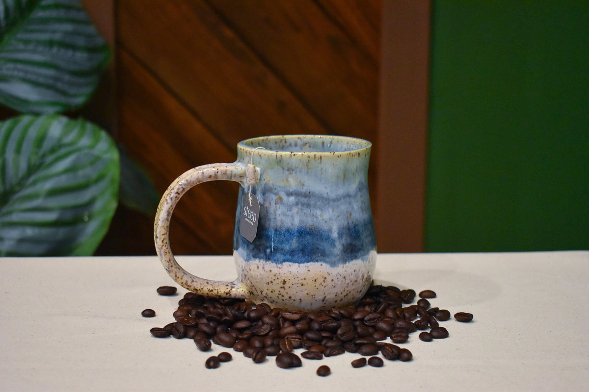 Hand-thrown mug in Sandbar, speckled teal rim over soft blue-grey and cobalt bands with a speckled cream base