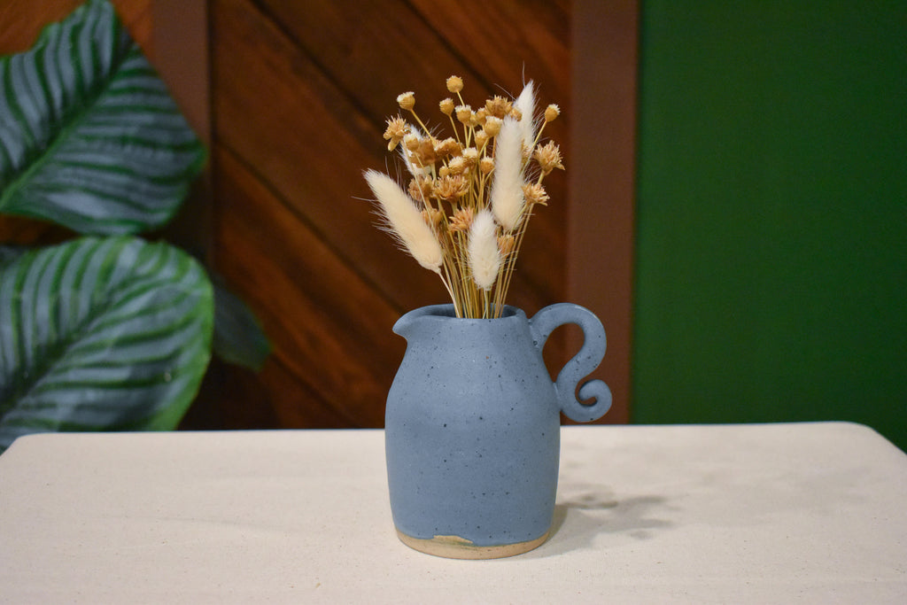 Small hand-thrown pourer in Stillwater with a spout and curled spiral handle, matte slate-blue glaze with raw clay at the foot