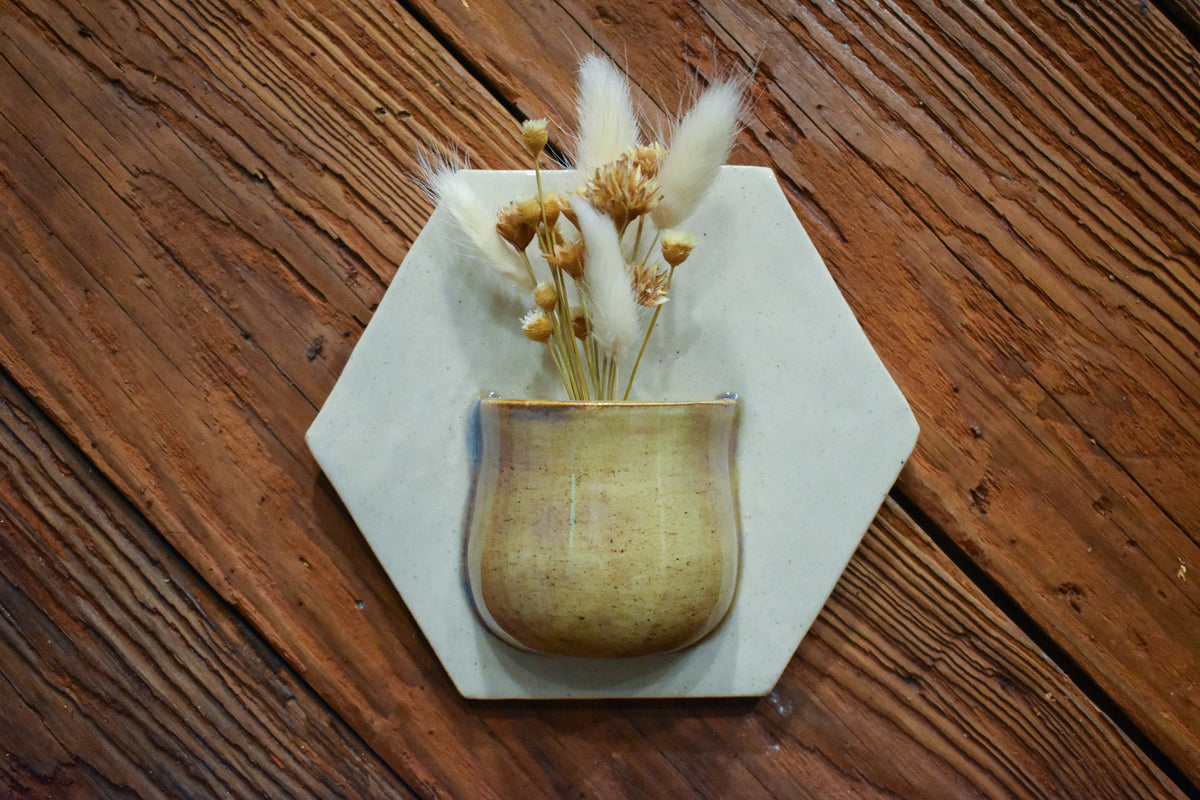 Small hand-formed bud wall vase in Honey, a glossy honey-gold pocket on a white hexagon back plate