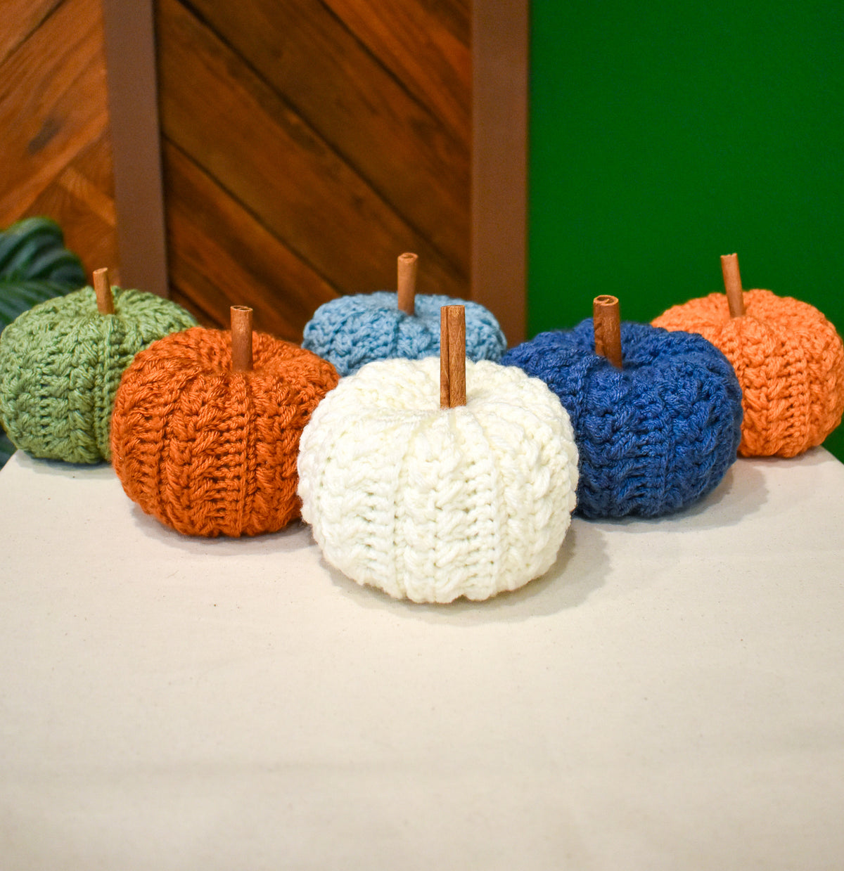 Six small hand-crocheted pumpkins with cinnamon-stick stems in Light Sage, Burnt Pumpkin, Sea Blue, Ivory, Country Blue and Desert Glaze