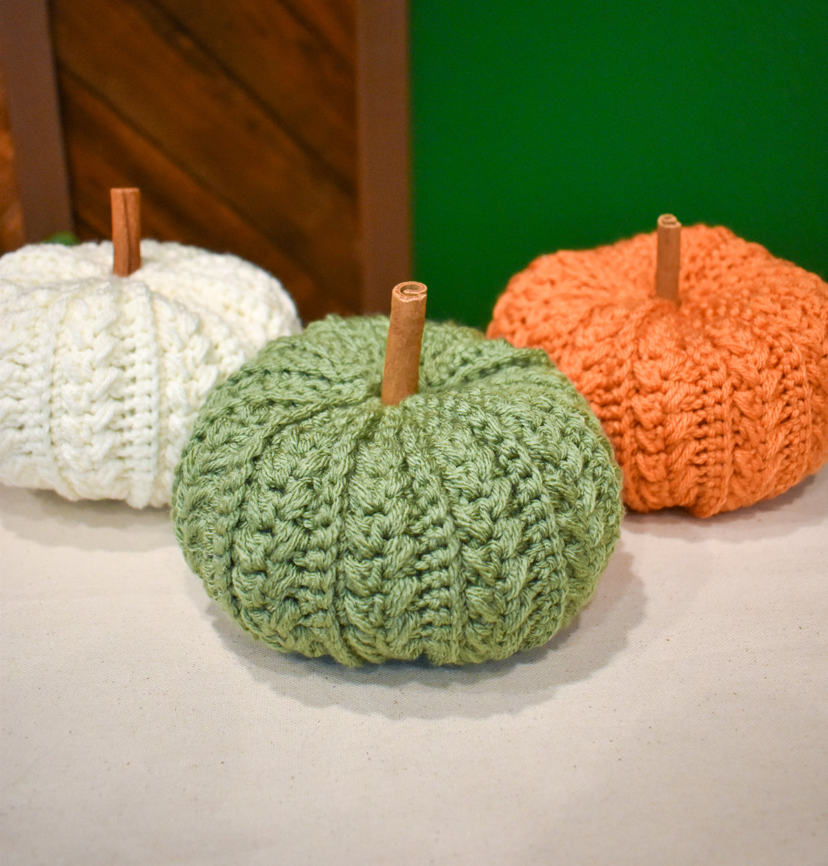 Three large hand-crocheted pumpkins with cinnamon-stick stems in Ivory, Light Sage and Desert Glaze