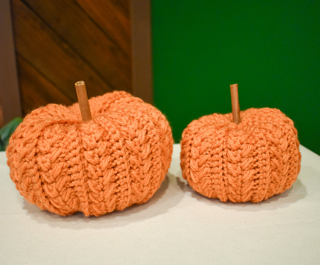 Large and small hand-crocheted pumpkins in Desert Glaze, side by side, each with a cinnamon-stick stem