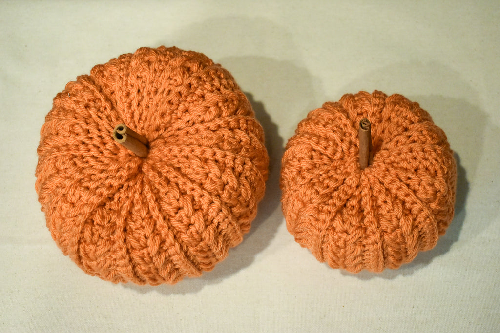 Top view of a large and a small hand-crocheted pumpkin in Desert Glaze, ribbed rows radiating from the stem